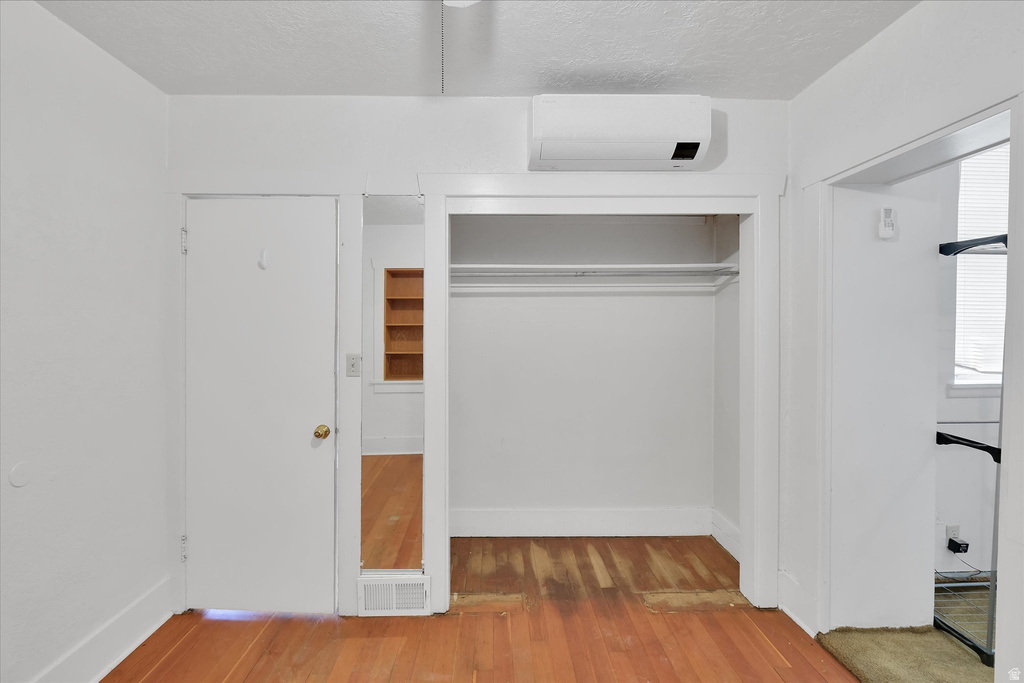 Built-in closet with hanging rod, wood-finish flooring, and a wall-mounted mini-split system