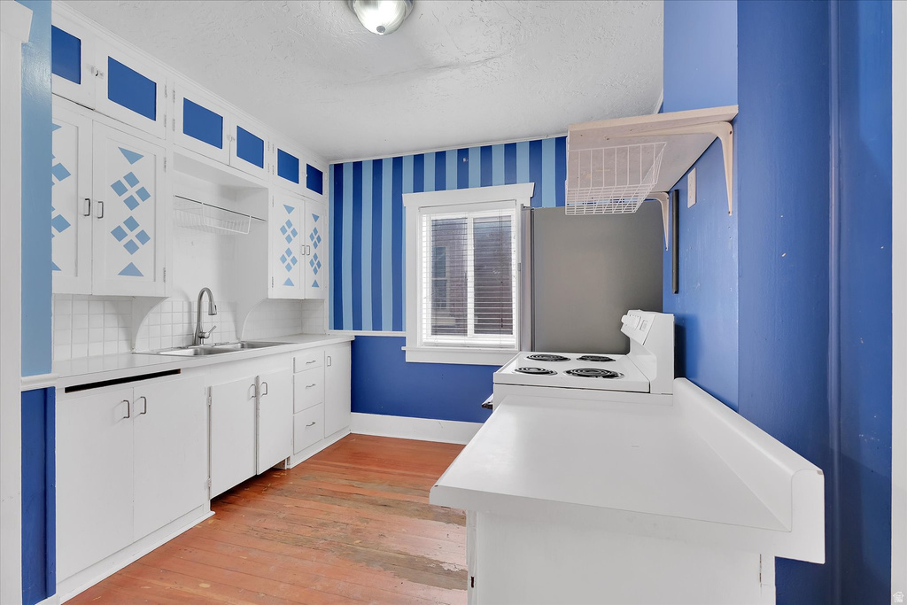 Kitchen featuring white cabinetry with blue accents, a stainless steel sink with a gooseneck faucet, white tile backsplash, and wood-finish flooring
