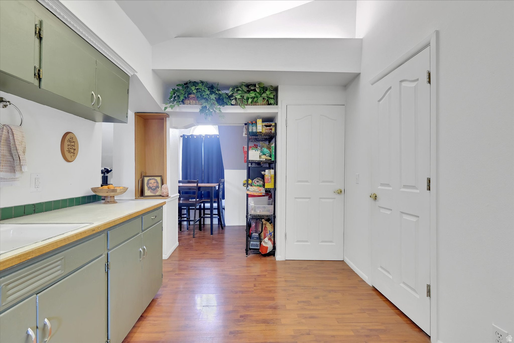 Kitchen area featuring wood-finish flooring, light green cabinetry, and white countertops with a green tile backsplash