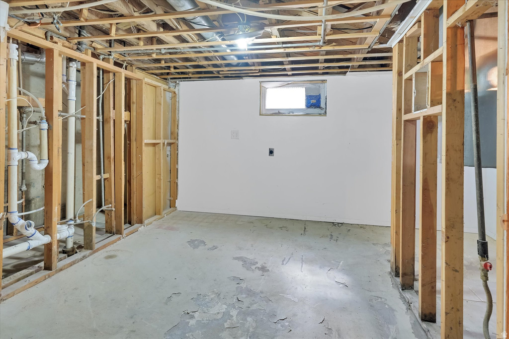 Unfinished basement with exposed ceiling joists and wood framing, featuring a small window and a concrete floor