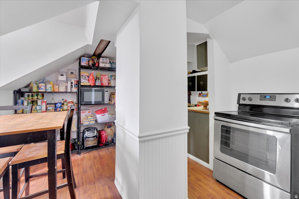 Kitchen area featuring wood-finish flooring, stainless steel range with a glass cooktop, and white beadboard paneling