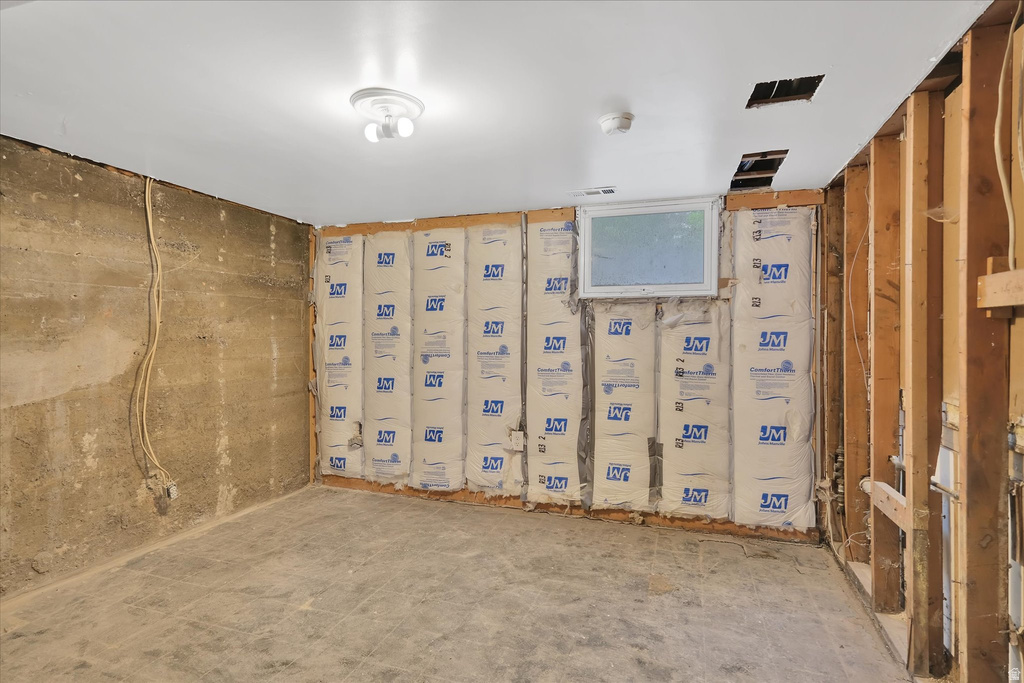 Unfinished basement space featuring exposed concrete walls, wood framing, insulation, a ceiling-mounted light fixture, and a single window