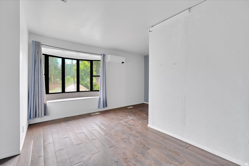 Spacious interior featuring a prominent bay window with a built-in window seat, wood-finish flooring, white walls, and a wall-mounted air conditioning unit