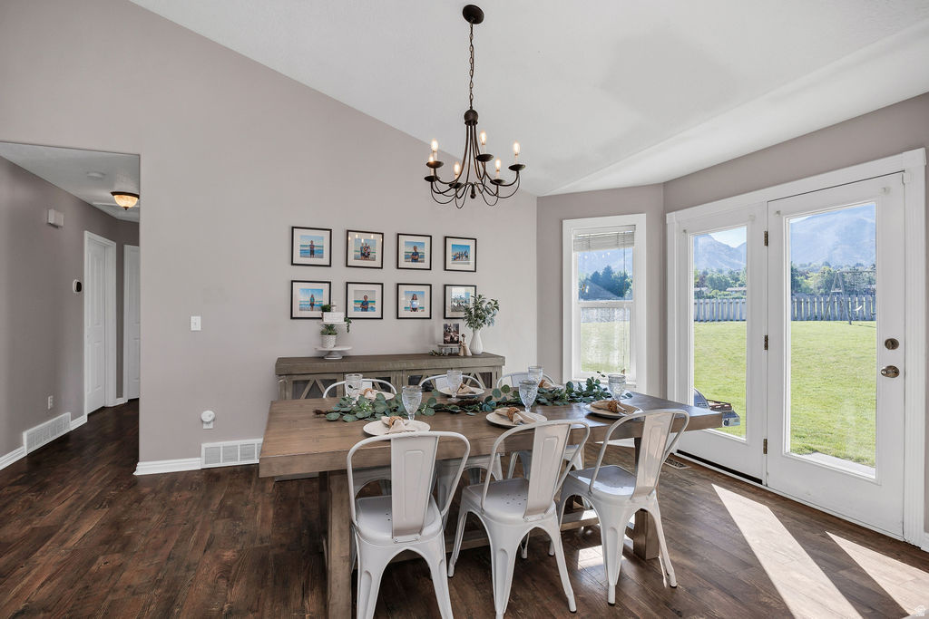 Dining area featuring wood-finish flooring, a contemporary chandelier, vaulted ceilings, and double French doors opening to the backyard