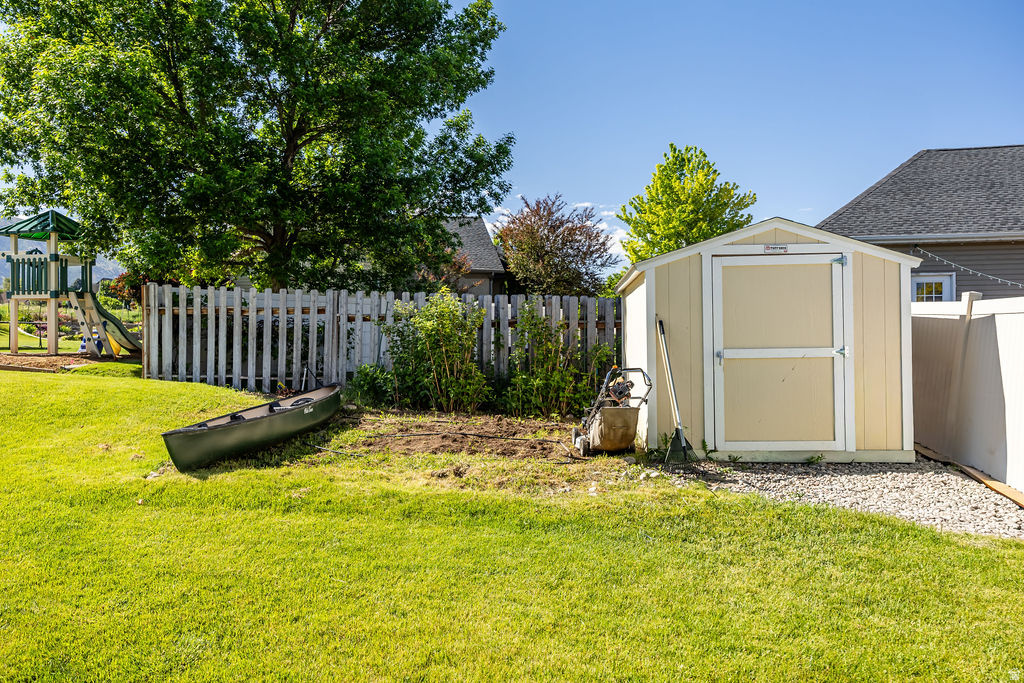 Expansive backyard featuring a manicured lawn, a detached storage shed on a gravel base, and a wooden picket fence