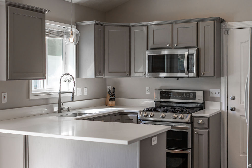 Kitchen featuring gray cabinetry, stainless steel appliances, a bar-height countertop, a single basin sink with a gooseneck faucet, and light-toned countertops
