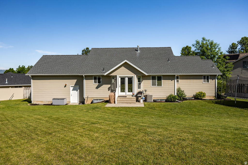 Expansive green lawn surrounds the rear exterior of the residence, featuring tan siding, a grey shingle roof, and a concrete patio