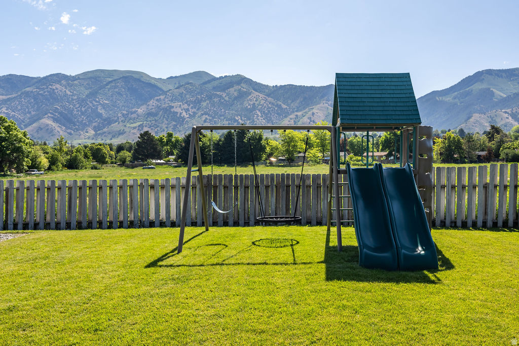 Expansive grassy yard featuring a wooden picket fence, a swing set with two swings, and a play structure with dual slides