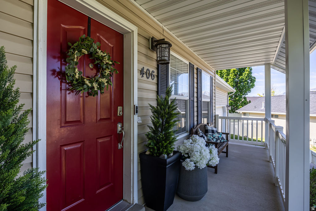 Inviting covered porch featuring a red panel door, light tan siding, white railings, a mounted outdoor light fixture, and dark window shutters