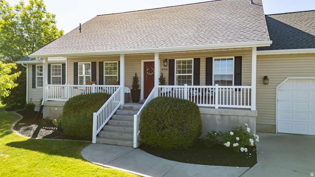 Beige siding exterior with dark shutters, covered front porch, asphalt shingle roof, concrete walkway, and an attached garage with a white door
