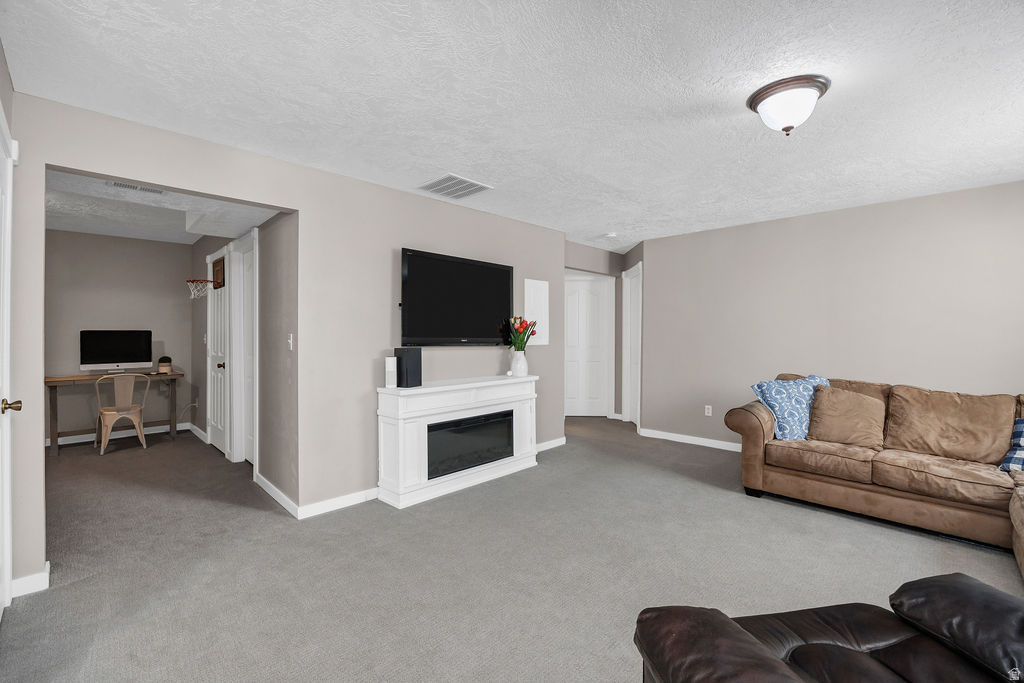 Spacious interior room featuring light gray walls, textured white ceiling, recessed lighting, and gray carpeted flooring