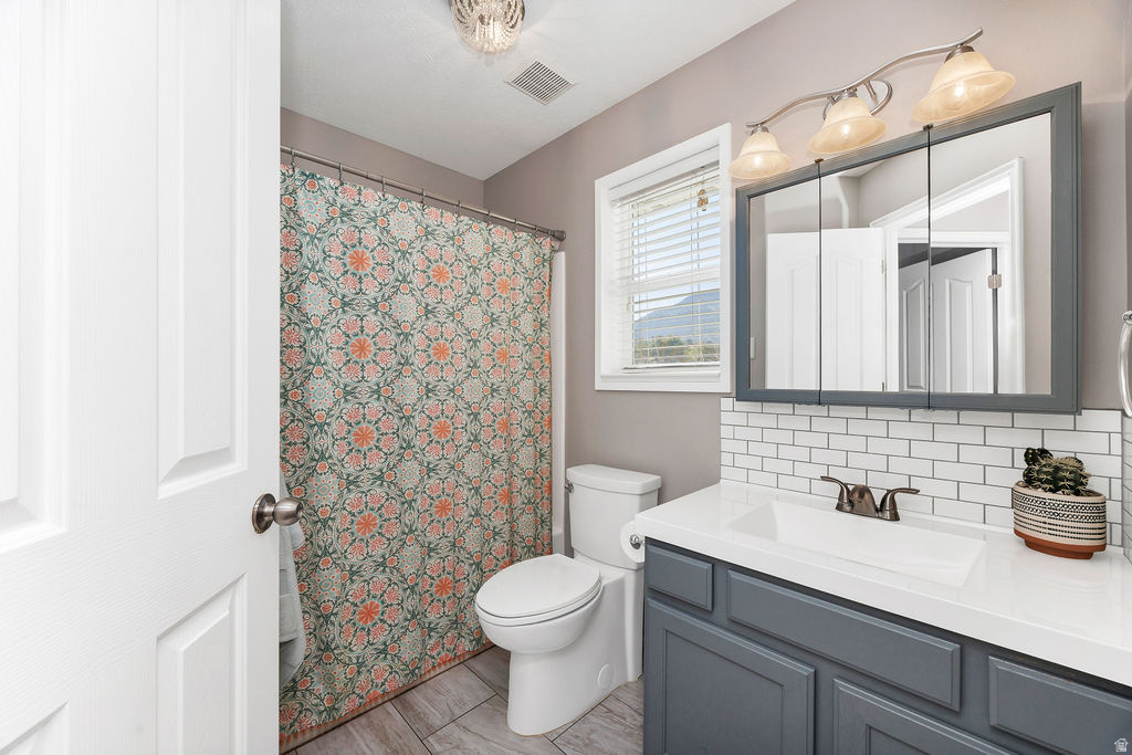 Bathroom featuring a built-in vanity with a white countertop and basin sink, dark gray cabinetry, and a white subway tile backsplash
