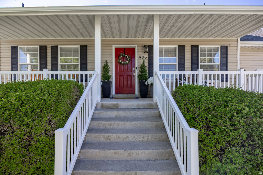 Covered front porch with concrete steps, white railings, and mature landscaping