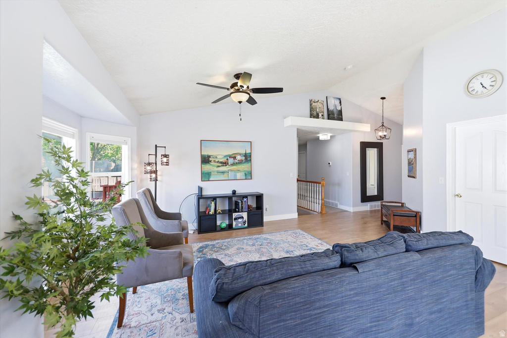 Spacious living area featuring vaulted ceilings, bay windows, a ceiling fan, wood-finish flooring, and a built-in shelving unit