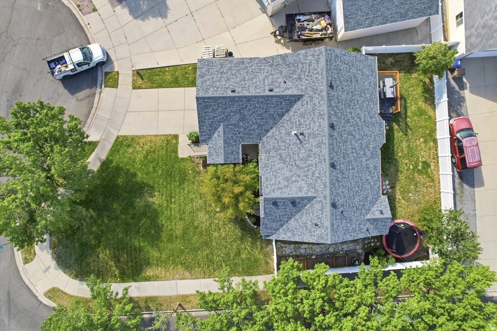 Residential property featuring a grey shingle roof, green lawn, concrete driveway, and mature trees