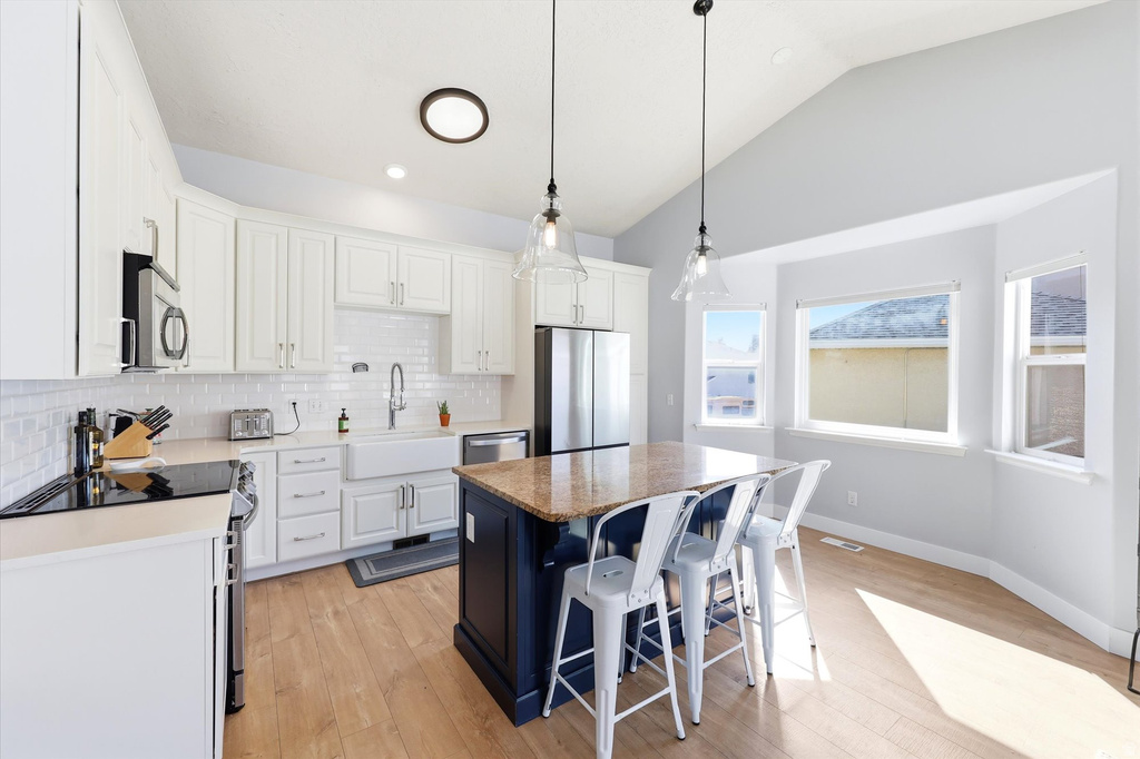 Modern kitchen featuring white shaker cabinetry, stainless steel appliances, a farmhouse sink, and a large central island with a granite countertop and pendant lighting