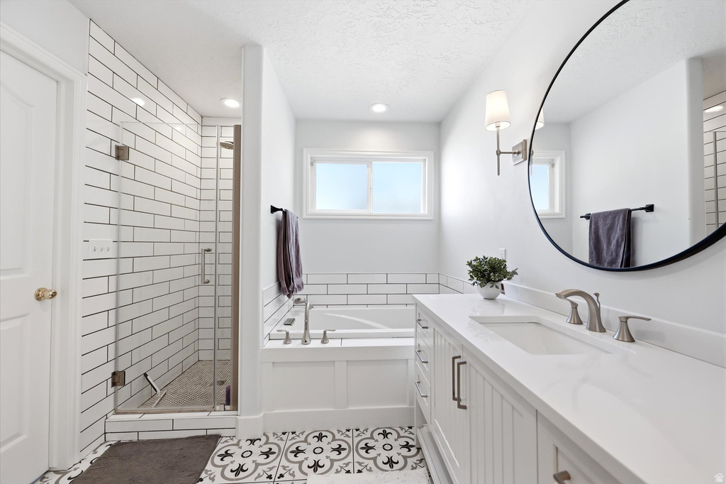 Modern bathroom featuring a double vanity with white cabinetry, a large circular mirror, a built-in tub with subway tile surround, a glass-enclosed shower with subway tile walls, and patterned floor tiling