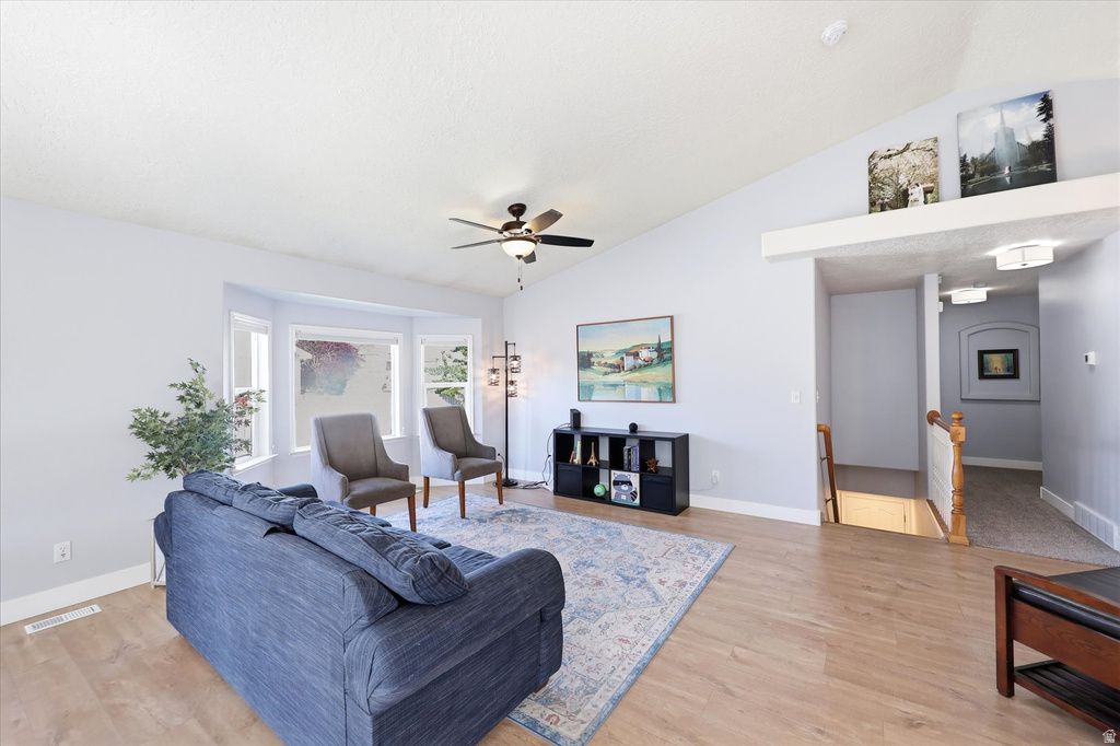 Spacious living area featuring light wood-finish flooring, a vaulted ceiling, and a ceiling fan with integrated lighting