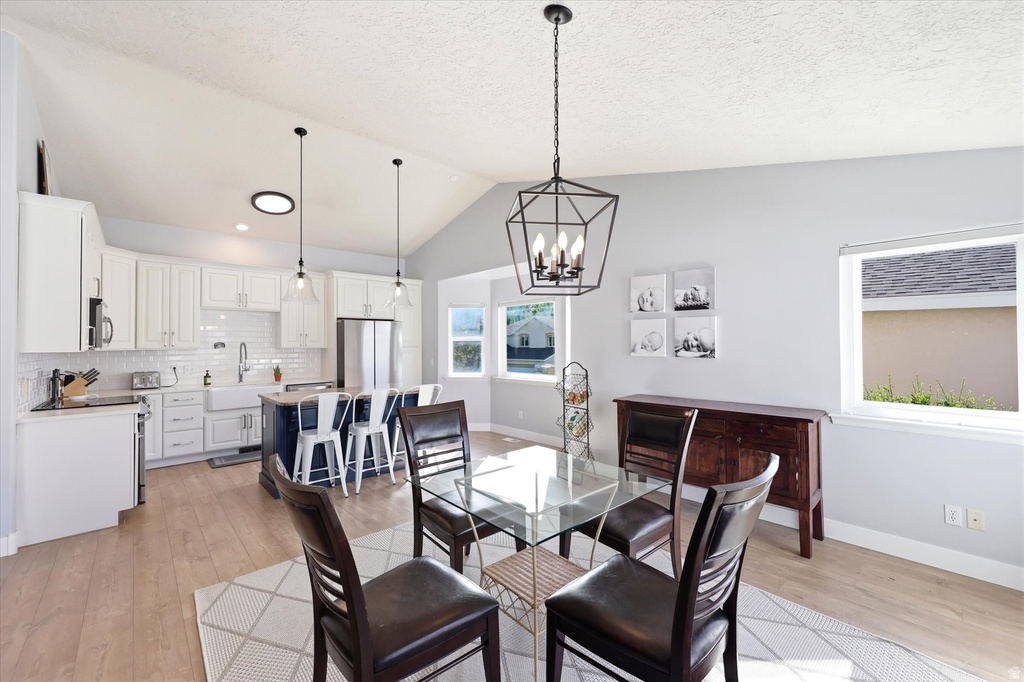 Open-concept kitchen and dining area featuring vaulted ceilings, wood-finish flooring, a kitchen island with seating, a farmhouse sink, and contemporary lighting fixtures