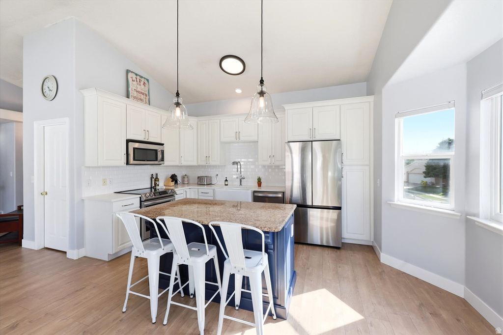 Kitchen featuring a central island with a granite countertop and contrasting base, white shaker-style cabinetry, stainless steel appliances, and wood-finish flooring