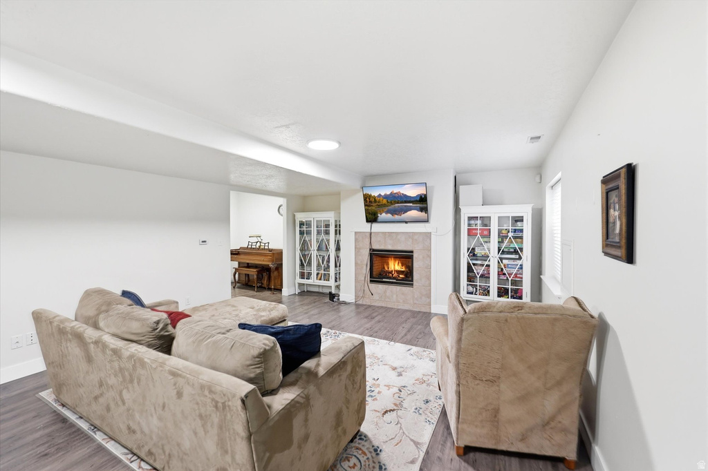 Living area featuring a fireplace with a light-toned tile surround and hearth, wood-finish flooring, and white walls