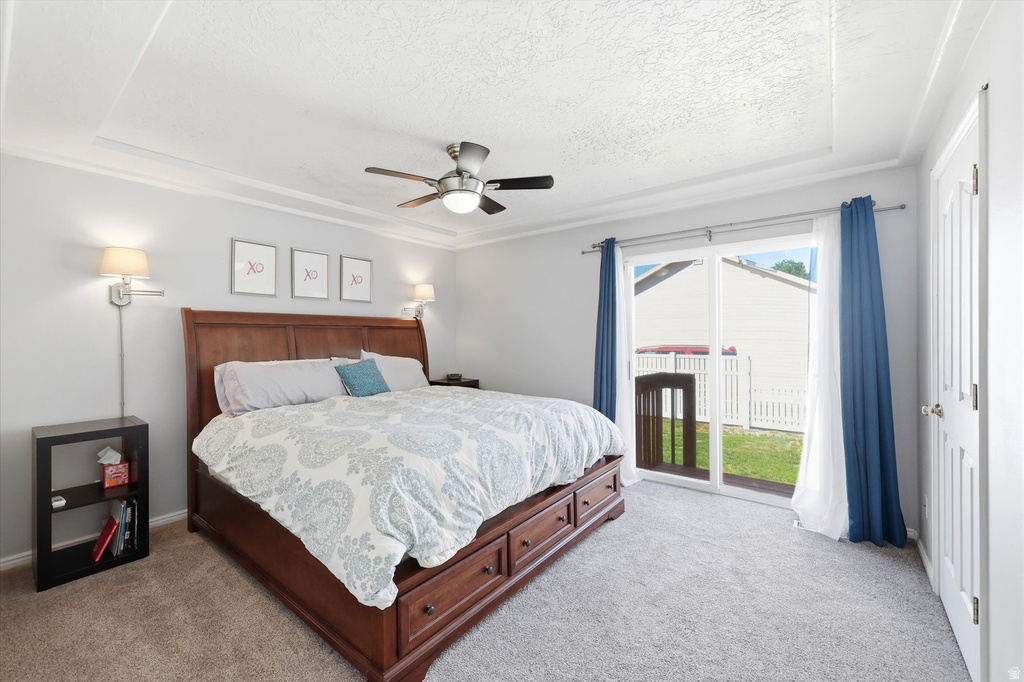 Bedroom featuring carpet flooring, a tray ceiling with a ceiling fan, and sliding glass doors providing outdoor access