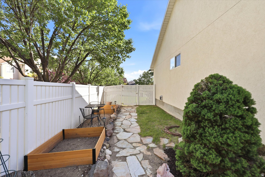 Side yard featuring a stone pathway, a raised garden bed, and a white privacy fence
