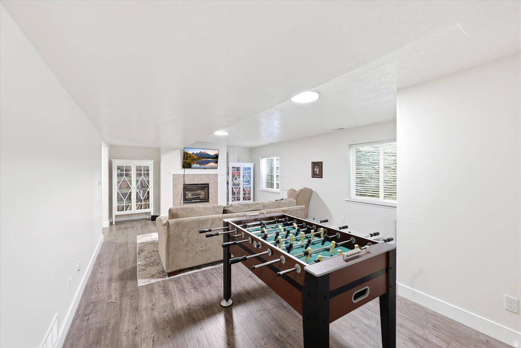 Spacious recreation area featuring wood-finish flooring, recessed lighting, and a fireplace with a light-toned surround