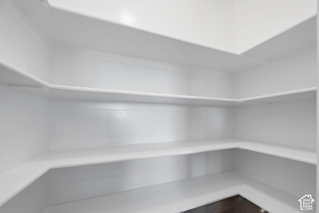 Walk-in pantry featuring multiple levels of white shelving and dark wood-finish flooring