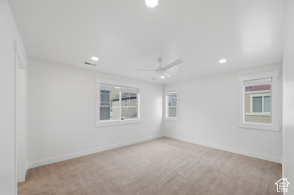 Spacious room featuring neutral carpet flooring, white walls, multiple windows with white trim, recessed lighting, and a ceiling fan