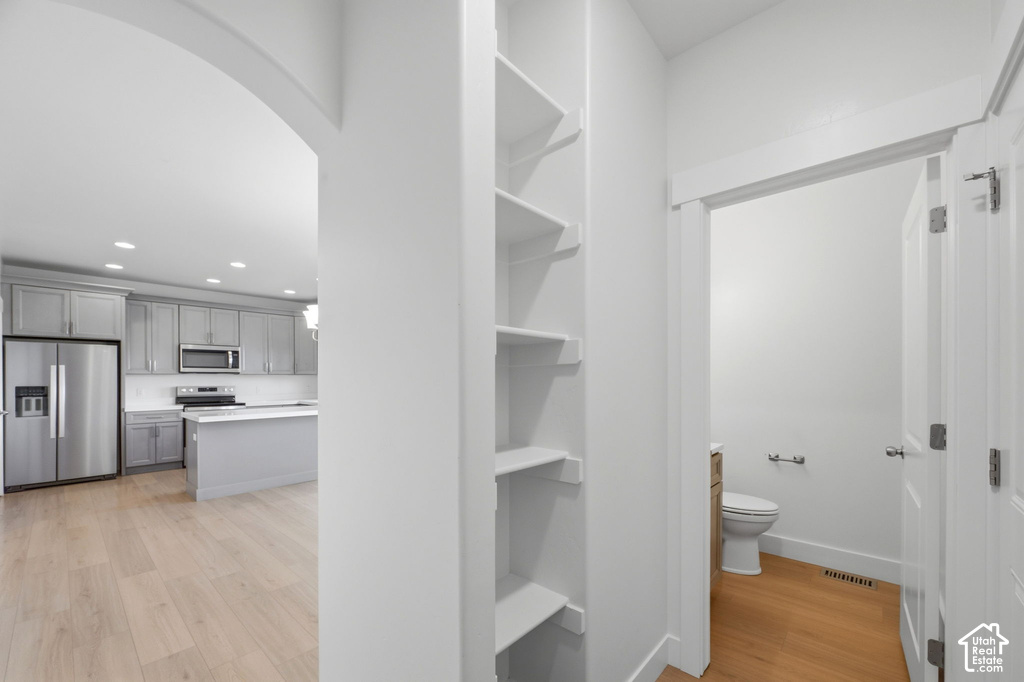 Archway entry to a modern kitchen featuring stainless steel appliances, grey cabinetry, and a center island with a white countertop