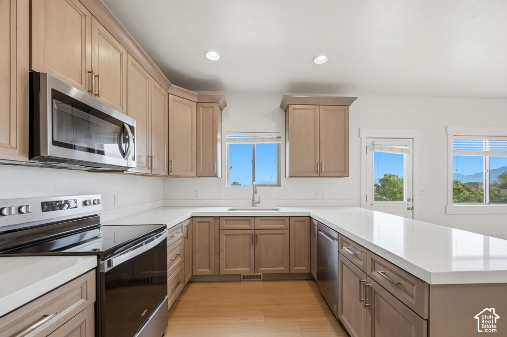 Kitchen featuring a U-shaped countertop layout with light-toned cabinetry, stainless steel appliances, and wood-finish flooring