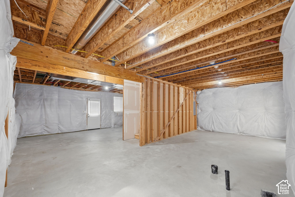 Unfinished basement featuring concrete flooring, exposed wood joists, and framed interior walls