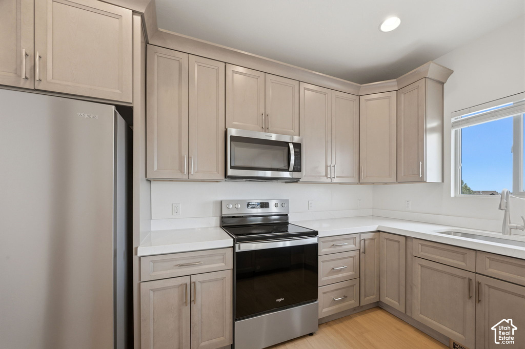 Modern kitchen featuring light wood-finish cabinetry, stainless steel appliances, white countertops, and a full-height white backsplash