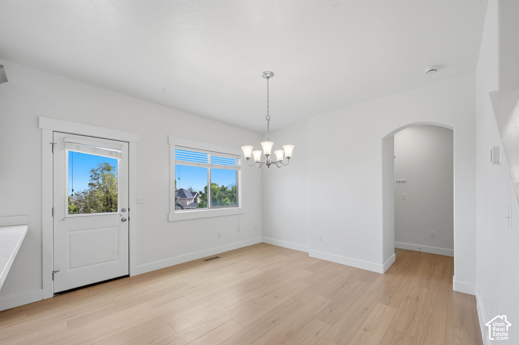 Bright open-concept space featuring light wood-finish flooring, white walls, and a contemporary chandelier