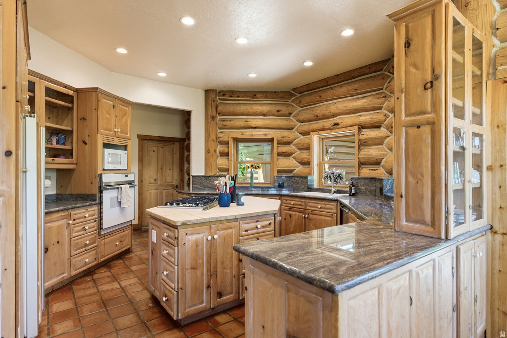 Rustic kitchen featuring log walls, tile flooring, wood cabinetry, stone countertops, and recessed lighting