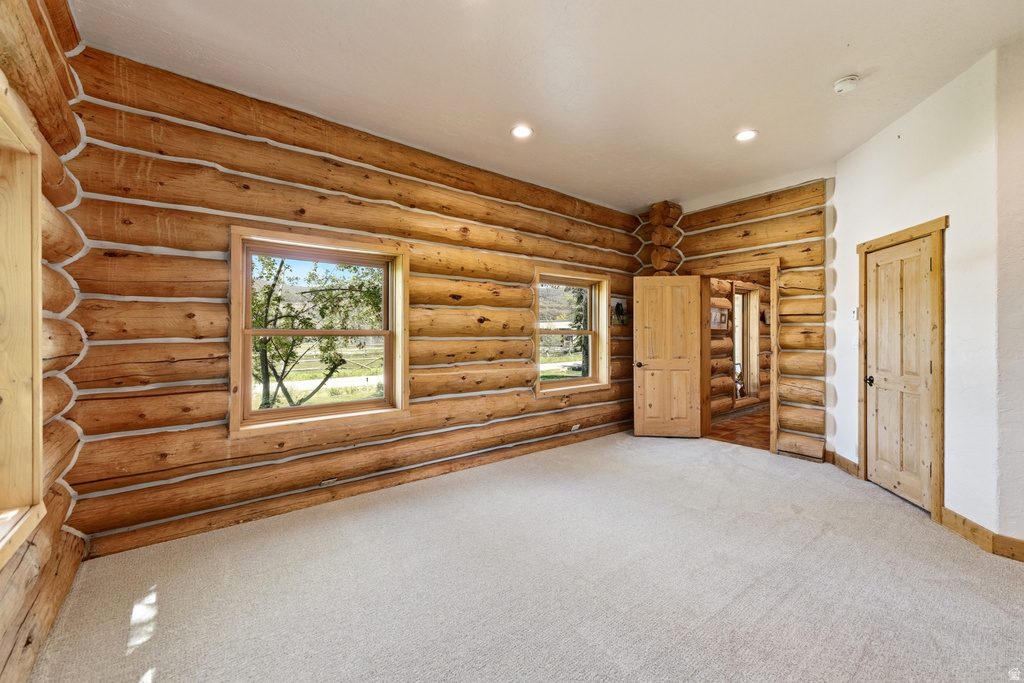 Room featuring log wall construction, multiple windows, light-toned carpeting, and natural wood doors