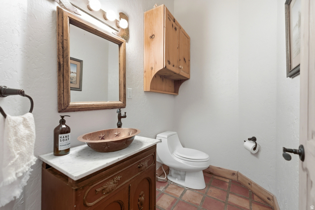 Bathroom featuring a copper vessel sink, dark wood vanity with a white countertop, and natural tone tile flooring