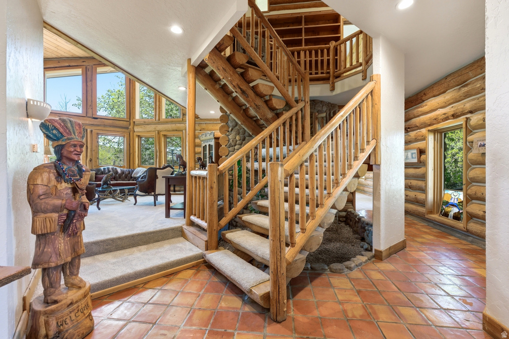 Rustic log staircase with carpeted treads and wood railings, complemented by terracotta tile flooring