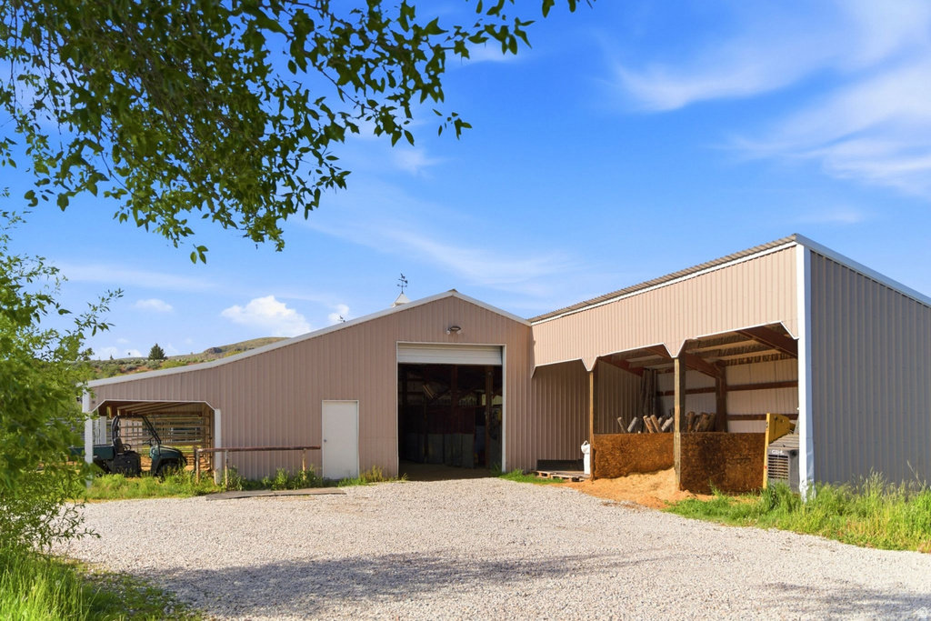Metal-sided barn featuring an expansive gravel forecourt, a large bay door, a side entry door, and two covered lean-to structures