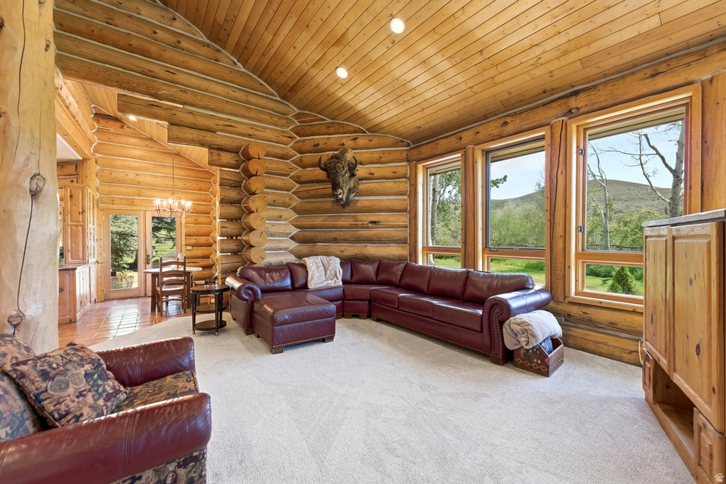 Spacious living area featuring log walls, wood-paneled ceilings, recessed lighting, and multiple large windows showcasing a natural landscape