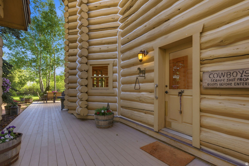 Log cabin exterior featuring a covered porch with wood-finish decking, a solid wood front door with a glass insert, and an exterior wall lantern