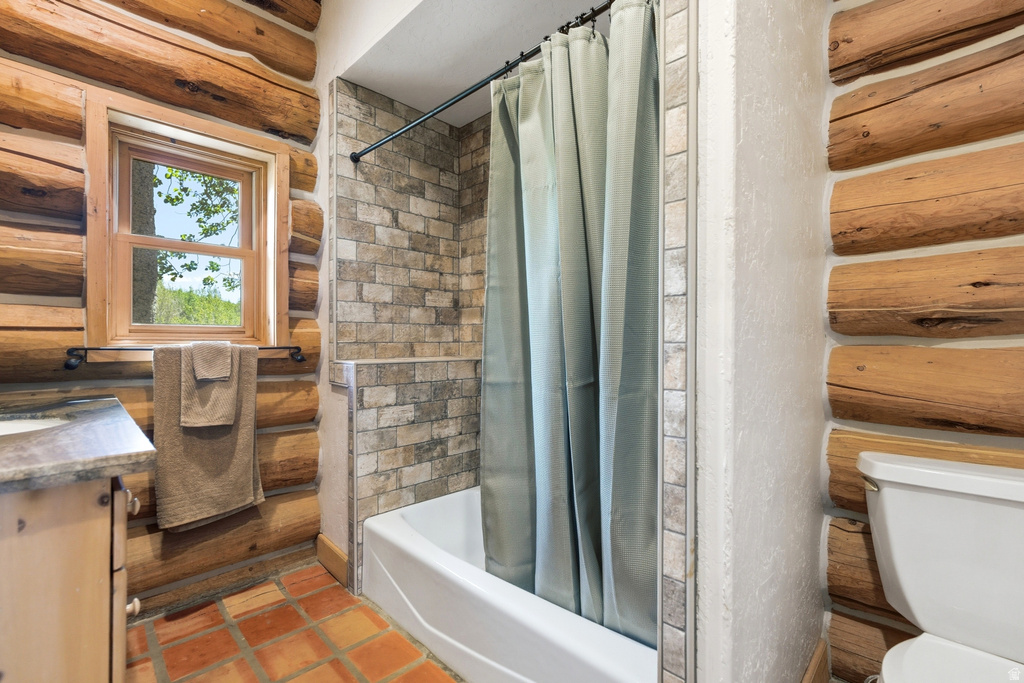 Bathroom featuring log walls, a window with natural light, a white bathtub with a tiled surround, and terracotta-style floor tiles