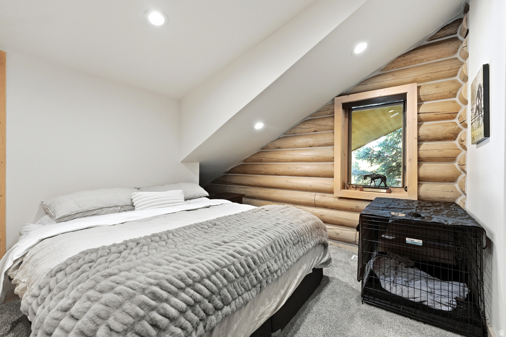 Bedroom with a sloped ceiling, showcasing recessed lighting and a window with wood trim