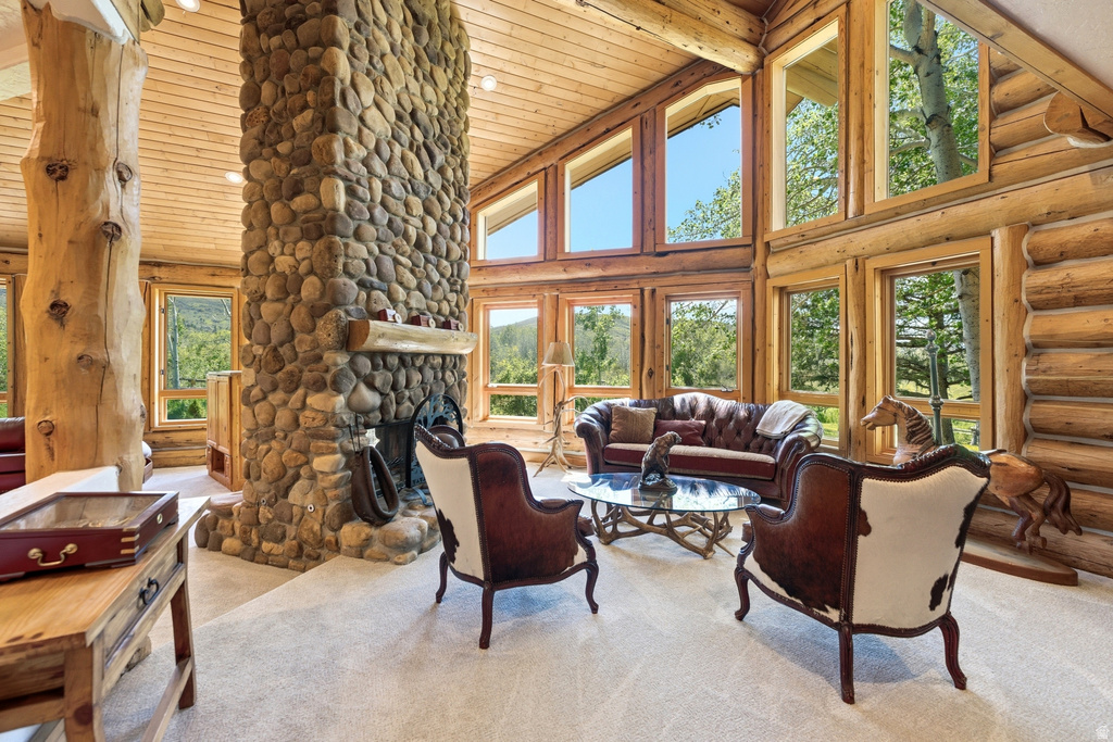 Great room featuring a floor-to-ceiling stone fireplace, natural log beam construction, wood-paneled ceilings, and light-colored carpeting