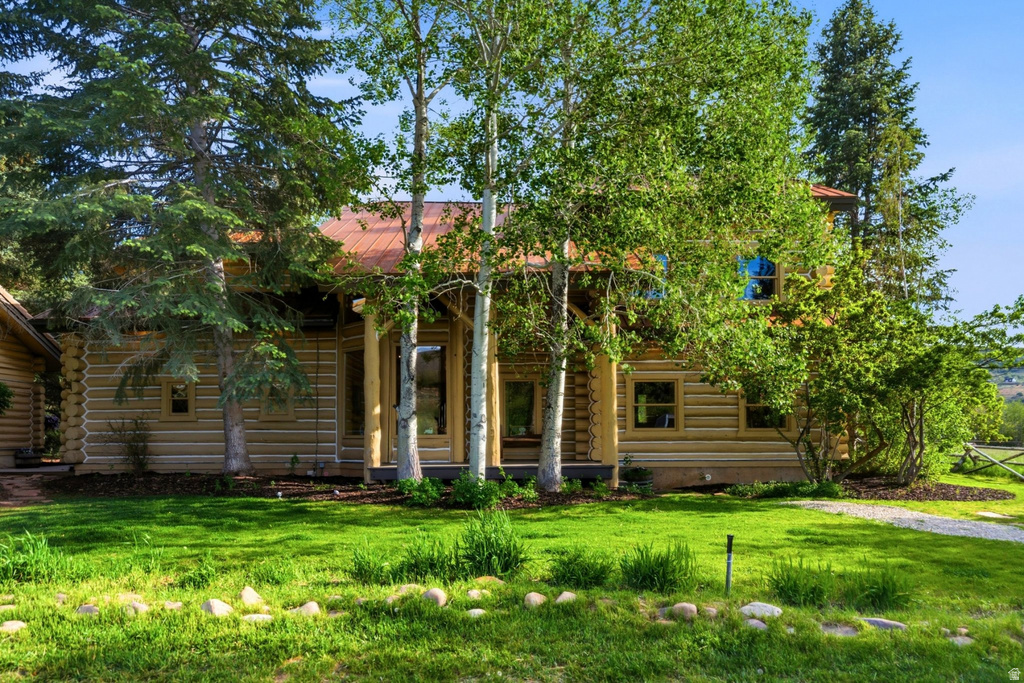 Log home exterior featuring a red metal roof, substantial wood columns, multiple windows, a stone-lined garden bed, and mature trees