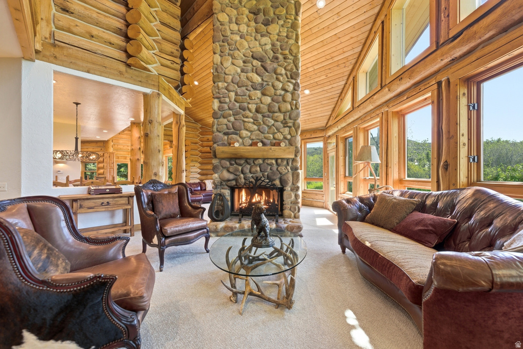 Great room featuring a floor-to-ceiling stone fireplace with a wood mantle, log walls, wood-paneled vaulted ceilings, and extensive window arrays