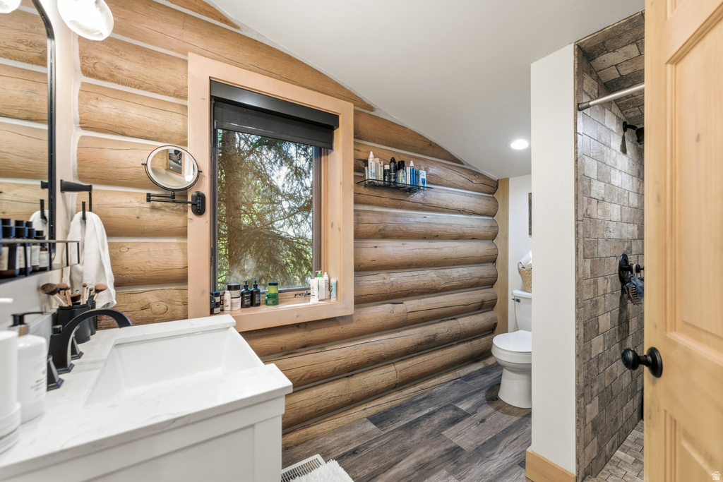 Bathroom featuring a white vanity with a rectangular sink and matte black fixtures, log-style wall paneling, wood-finish flooring, a window with natural wood trim, and a tiled shower enclosure