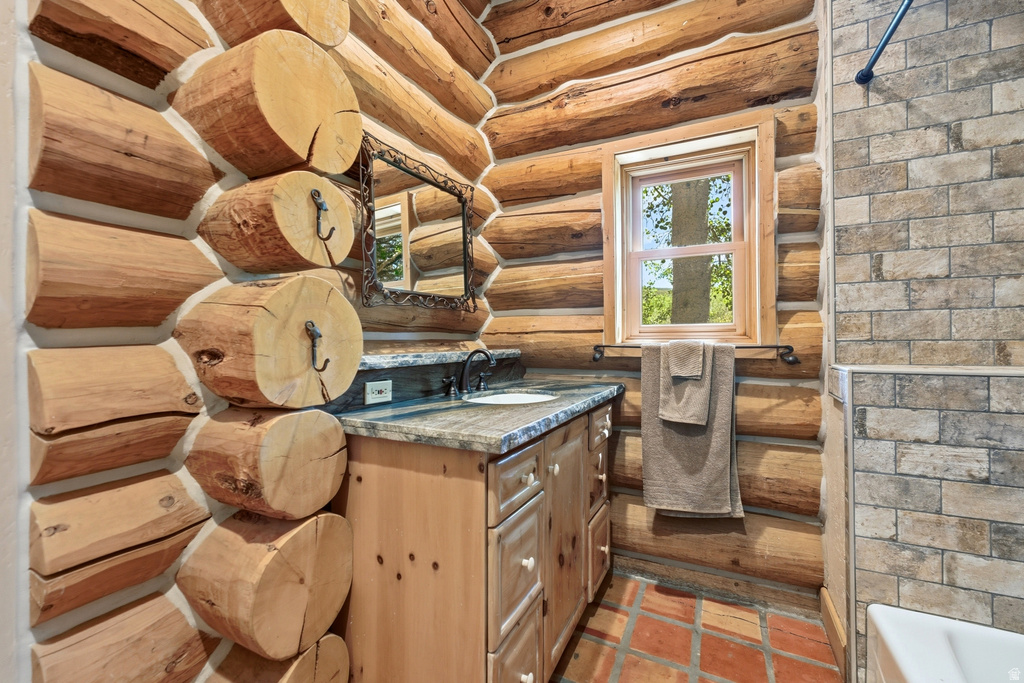 Log cabin interior featuring a wood vanity with a stone countertop, a window with natural light, tiled flooring, and a tiled shower surround