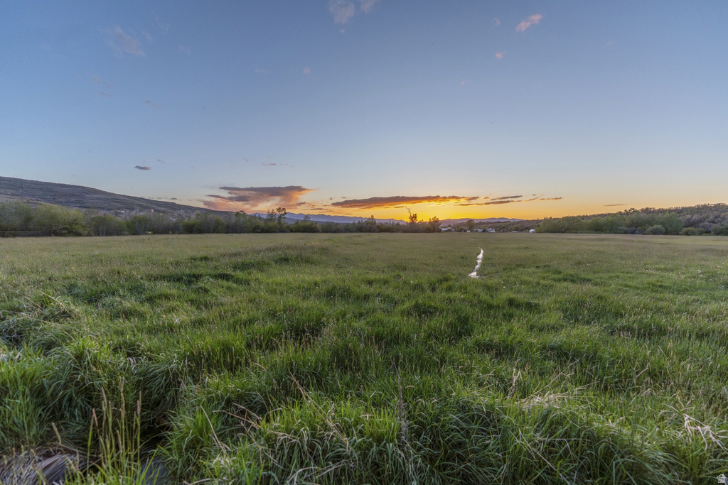 Expansive green field with natural grass, framed by distant hills and a vibrant sunset horizon